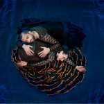 Male and female dancers, in lace tops and long ruffled skirts, intertwine into a circle formation shot from above