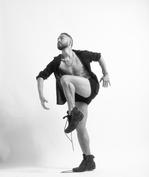  A male-identifying Asian dancer in a pose wearing an open black button up shirt, black shorts, and black boots.