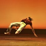 solo male performer in red top and khaki pants floats in midair