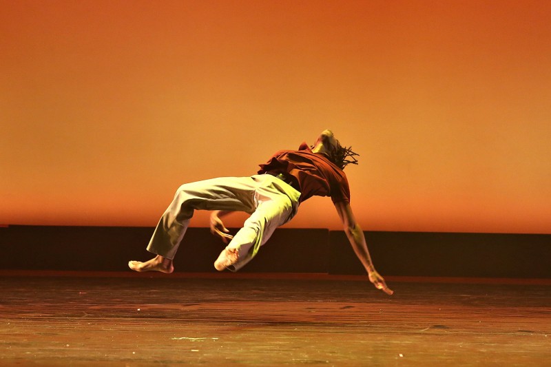 solo male performer in red top and khaki pants floats in midair