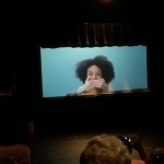 A Black Woman with big beautiful hair has her mouth covered by two white hands.