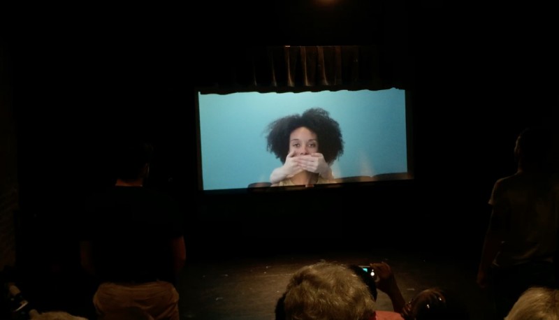 A Black Woman with big beautiful hair has her mouth covered by two white hands.