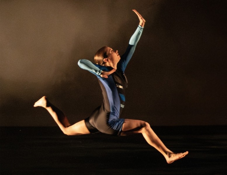 Dancer leaping with bent knees and flexed feet while reaching in profile