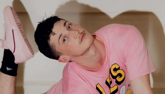 A photo of Ash Yergens head tilted to the side looking at the viewer with a light pink shirt on.