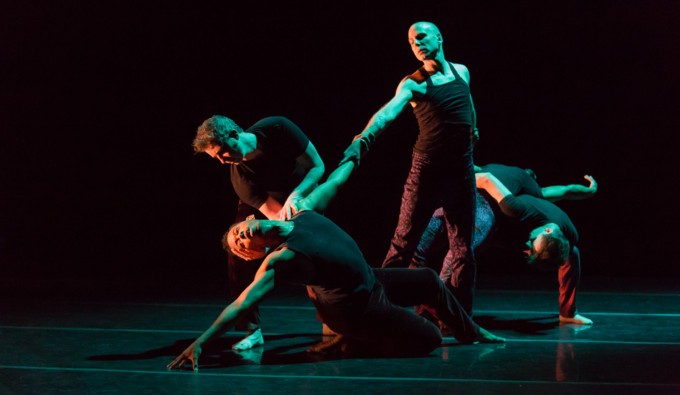 Five performers on the stage with dark lighting. The performers form a 90 degree triangle as though someone is falling.
