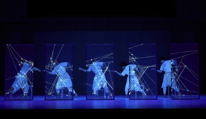 Five dancers from "discrete figures 2019" in white clothing in profile making geometric shapes behind transparent screens.