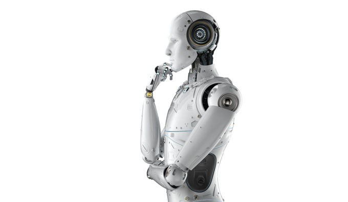 A white robot with its arms crossed and hand to mouth in front of a white back drop.