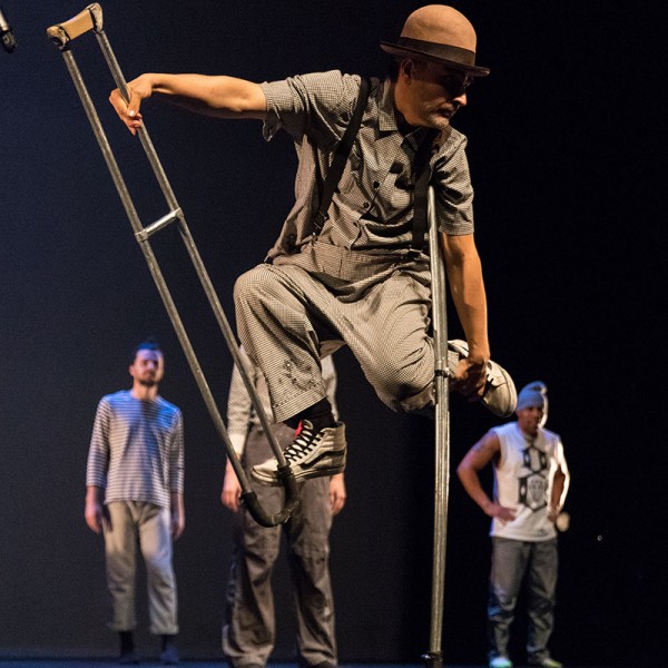 A white man in a brown hat balancing himself on two crutches to suspend himself in the air.