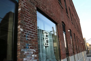 Image shows the Eyebeam office brick building, with our logo "E" neon sign in the window