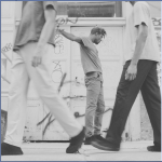 One African-America Dancer standing near a tagged wall of graffiti surrounded by other male dancers.