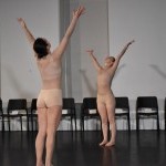 two dancers in nude costumes face each other with their arms raised