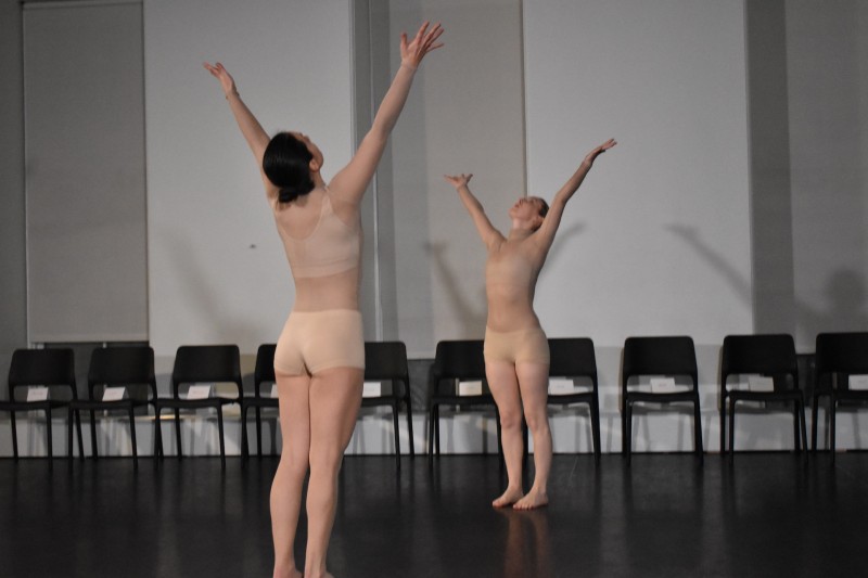 two dancers in nude costumes face each other with their arms raised