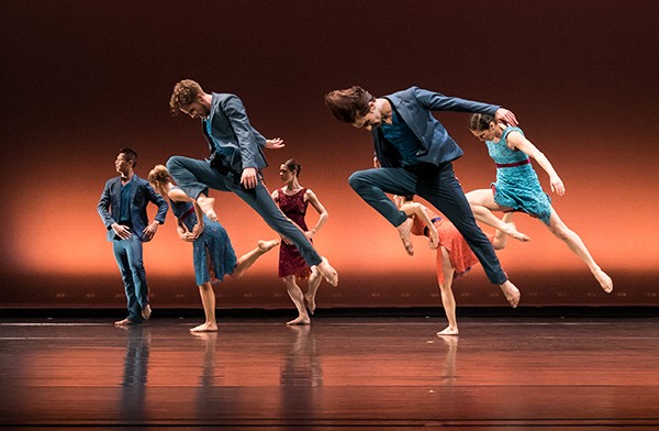 Seven dancers leaping across the stage.