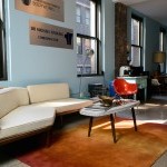 Photo of the studio with light blue walls, lots of windows, a tan couch and an orange carpet.