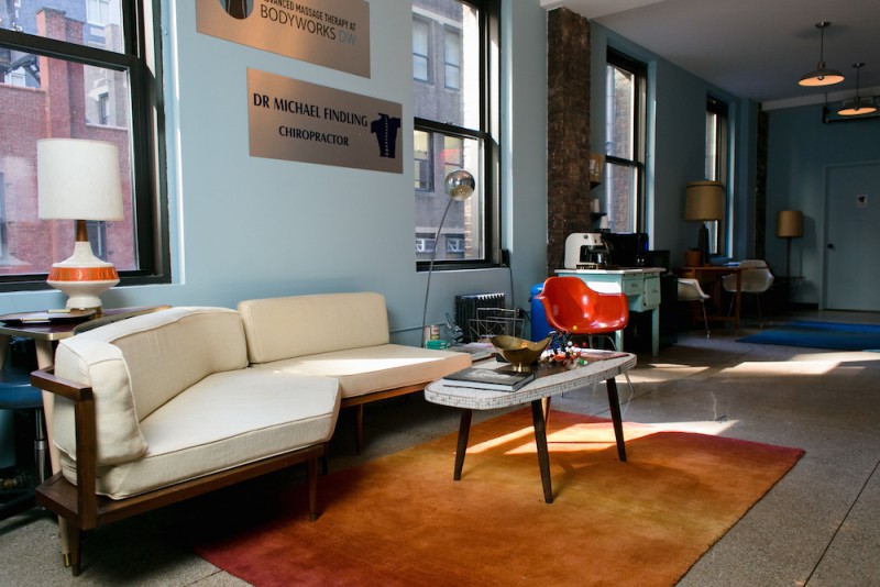 Photo of the studio with light blue walls, lots of windows, a tan couch and an orange carpet.