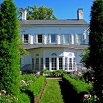 The back of Morven's large white house and garden on a sunny day.