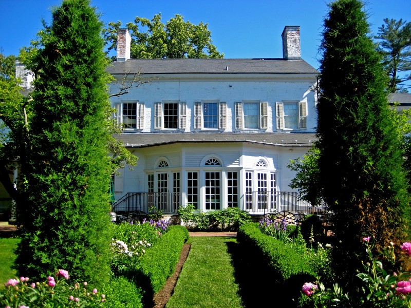 The back of Morven's large white house and garden on a sunny day.