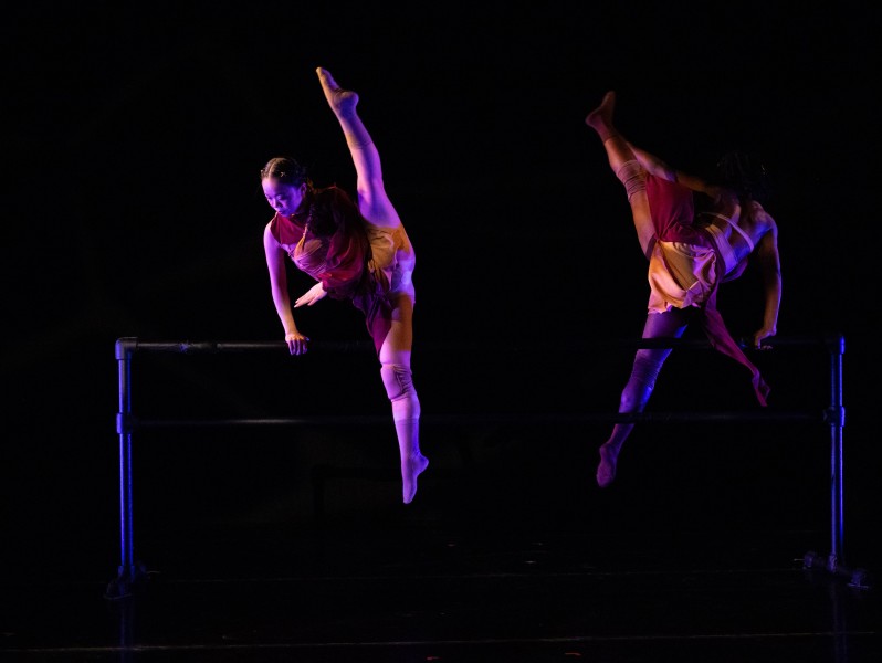 An Asian woman jumps over a ballet barre with a 180 split