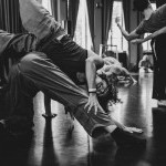 black and white image of one dancer balanced over top of another, legs in the air