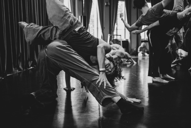 black and white image of one dancer balanced over top of another, legs in the air