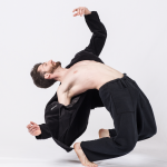 Dancer in black pants and black jacket in a hinge