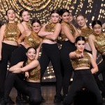 Group of young dancers posed around each other with gold sequin top and black bottoms. 