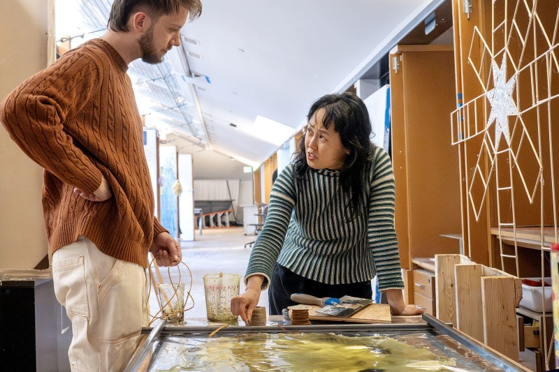 Woman speaking to a young man about artwork on a table.
