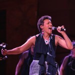 Woman singing into a microphone holding a tamborine