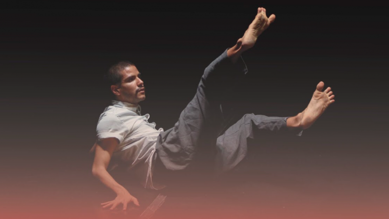 Man on the ground with his feet and chest in the air. He is wearing two tones of grey, darker pants and lighter shirt.