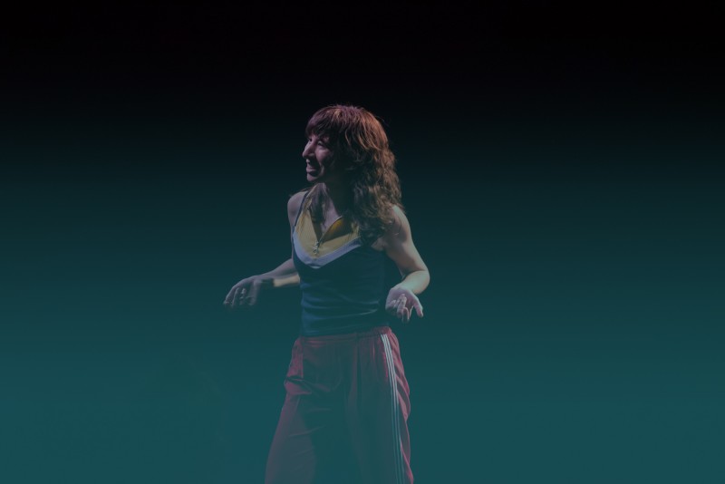 Women with brown hair wearing red pants and a navy tank top. She is in the middle of gesturing a question with her hands. 