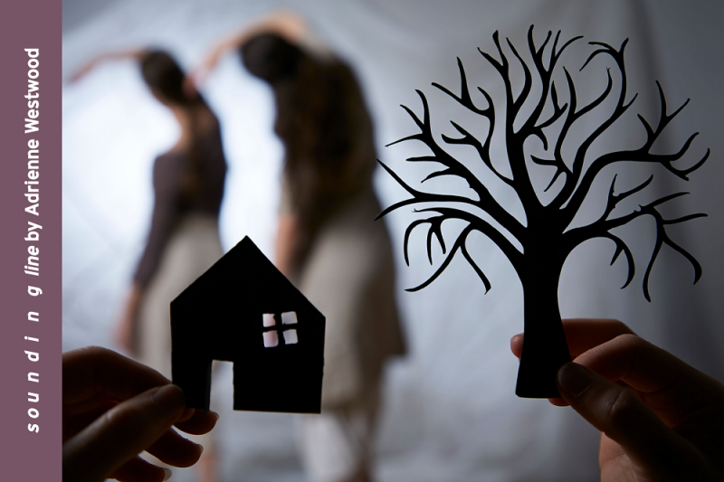 Paper cutouts of a house and a tree with dancers in background