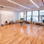 sunny studio with hardwood floors, a massage table, windows, a whiteboard, and stools