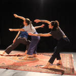 Three dancers, two in the foreground with arms outstretched & one partially visible behind, are dancing on a rug at the BAC