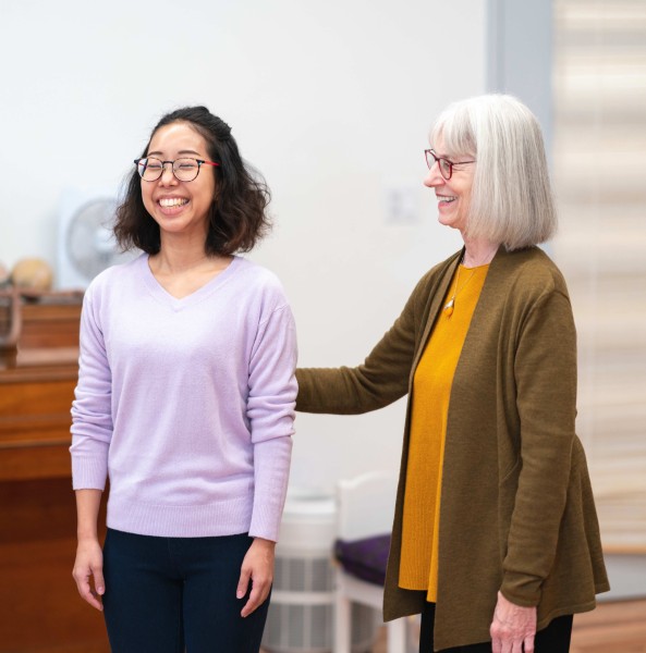 A student in purple smiling while receiving hands-on from a trained Alexander Technique teacher