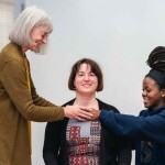 Two AT teachers are using hands on with a student to guide them to a better balance. Teachers and student are smiling.