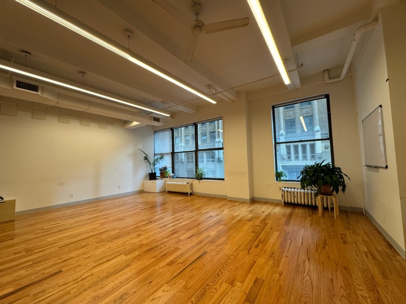 Spacious empty room with wooden floor, windows, and plants