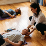 A student laying semi-supine on the floor while and Alexander Technique teacher has her hands on her head.