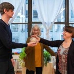 A smiling Alexander Technique teacher guiding two teacher trainees to pass a ball back and forth with good use and awareness. 