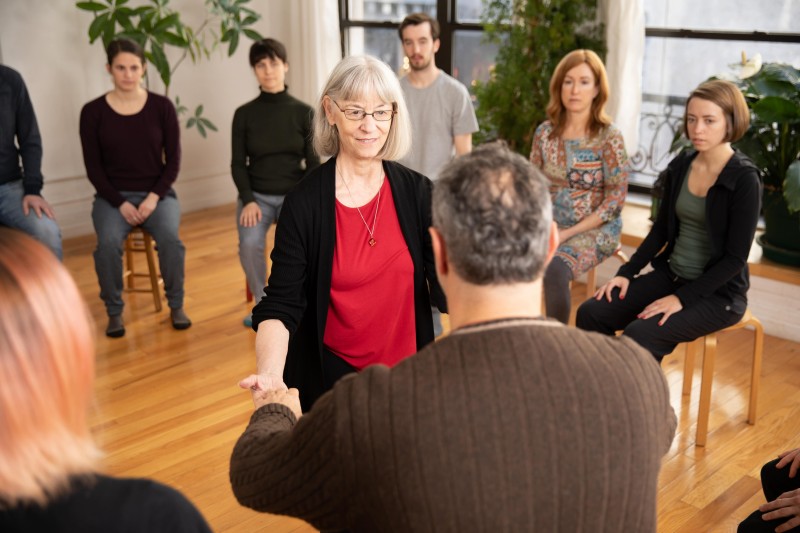 An Alexander Technique teacher using her hands to gently guide a student toward a standing position from sitting. 