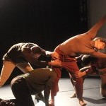 3 dancers grab the legs of a 4th dancer who is standing and reaching her body sideways during a performance at the BAC