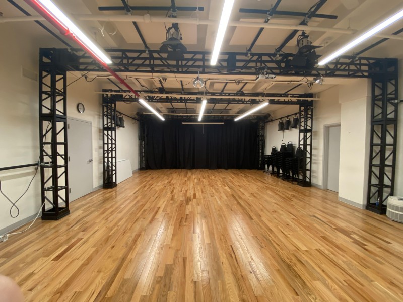 The Karl Kemp Performance Space, with a black curtain and hardwood floors and a lighting grid