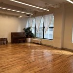 sunny studio with a piano, hardwood floor, and windows with white curtains