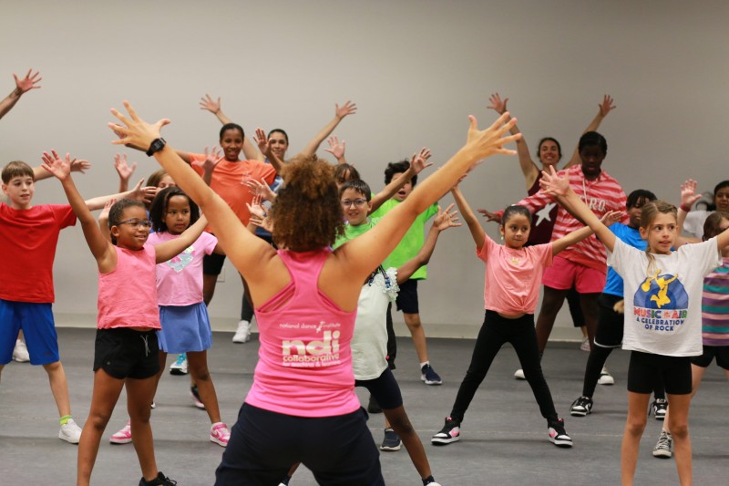 A teacher and students raise their arms above their heads.
