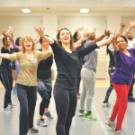 Teaching artists facing the camera and posing with their arms extended forward in a dance studio
