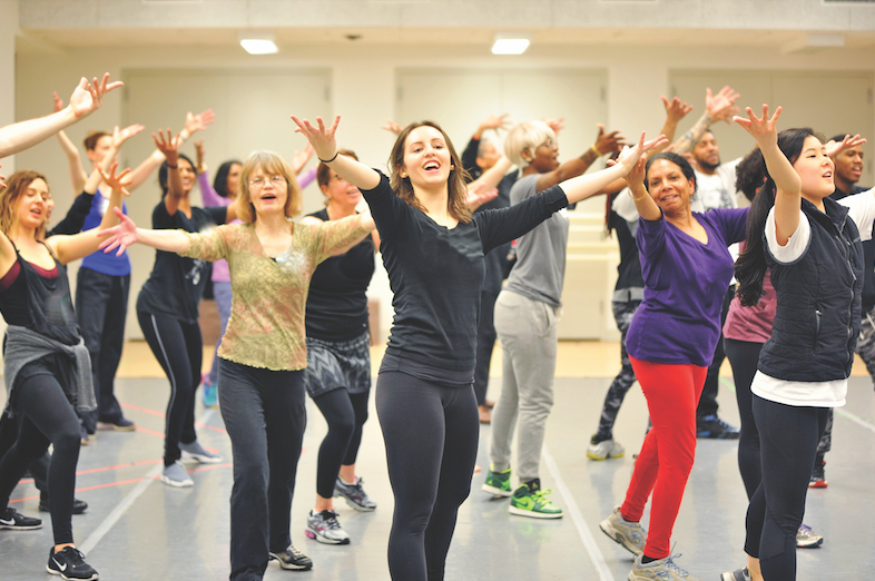 Teaching artists facing the camera and posing with their arms extended forward in a dance studio