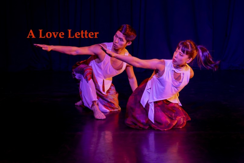 Two Asian dancers wearing red and white, kneel with their right arms out to the side. 