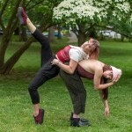 Charly and Eriel Santagado in a weight sharing pose in a park. Dancers are wearing red, gray, and white, with sneakers.