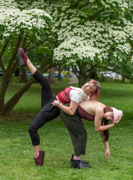 Charly and Eriel Santagado in a weight sharing pose in a park. Dancers are wearing red, gray, and white, with sneakers.