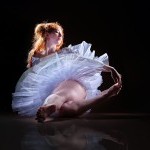 Ballerina sitting illuminated from behind with a glow around the shilouette
