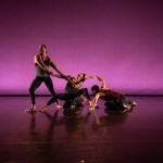 Photo of four male dancers on stage with purple backdrop lighting